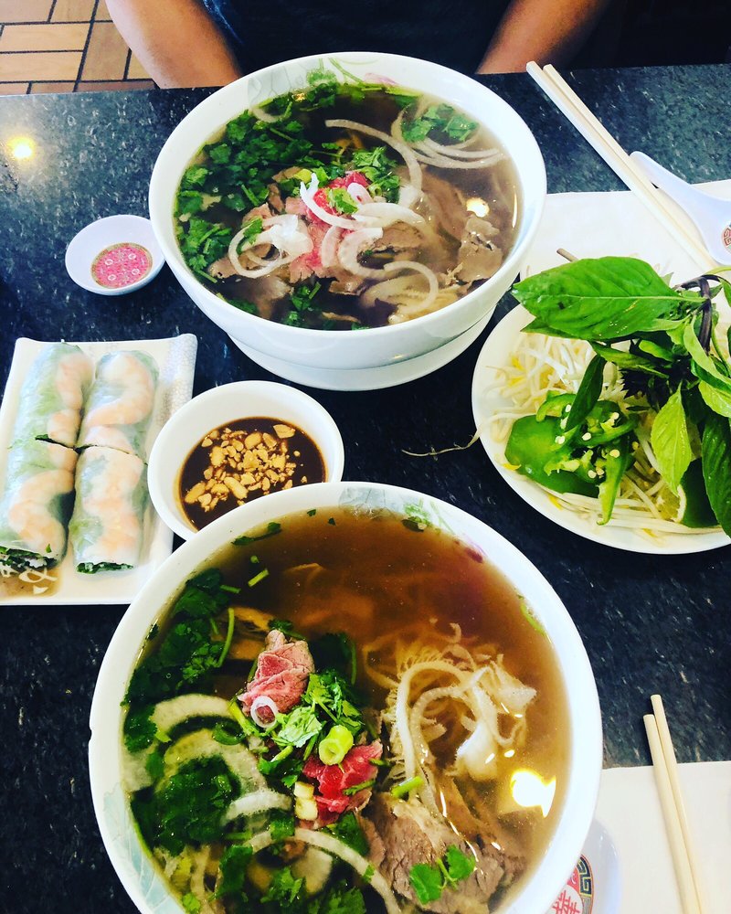 Two bowls of pho with fresh spring rolls, herbs and lime